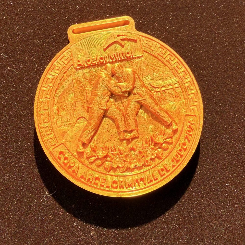 Medalha dourada da Copa ArcelorMittal de Judô, com a marca ArcelorMittal e dois judocas em relevo.