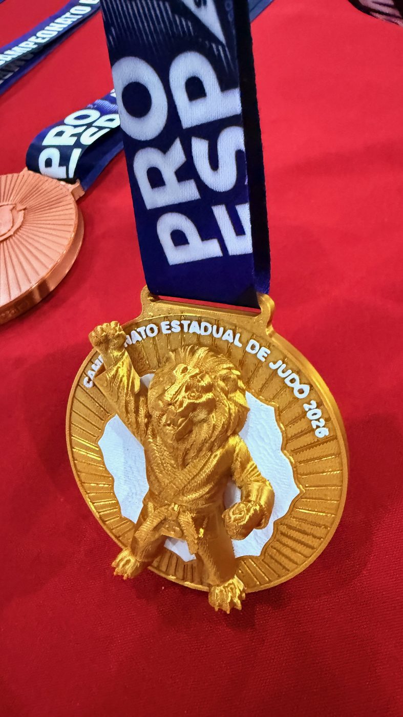 Medalha kids do Estadual de Judô 2026 com um leão judoca esculpido em volume sobre o disco.
