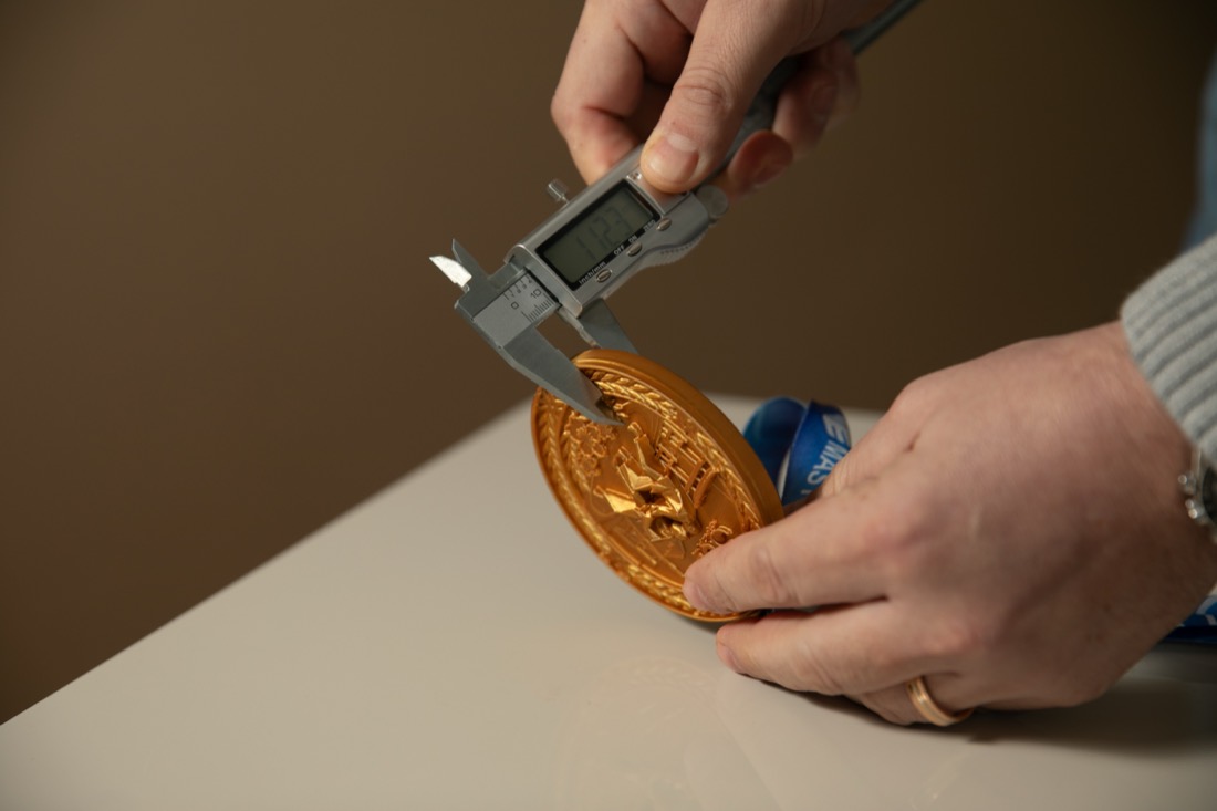 Paquímetro digital medindo a espessura de uma medalha dourada.