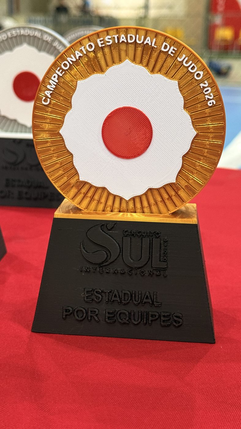 Troféu de disco dourado com hinomaru branco e vermelho em relevo, sobre base preta gravada Estadual por Equipes.